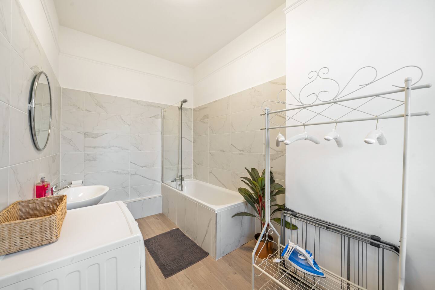 Modern bathroom setup in Shepherd’s Bush with a toilet, wall-mounted sink, heated towel rack, large mirror, white walls and wood-textured flooring. Just minutes from Notting Hill, it’s a fresh, functional space in West London’s vibrant heart.