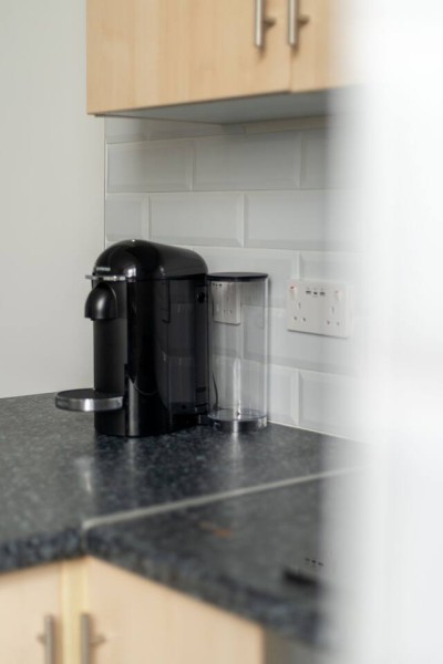 Coffee station on sleek counter with subway tiles and wood cabinets.