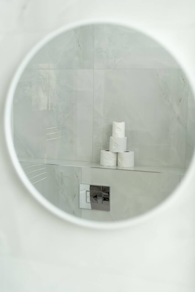 Mirror view of stacked toilet rolls in sleek marble-tiled bathroom.