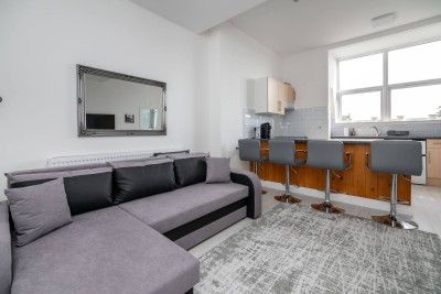 An inviting living area with natural light, an L-shaped sofa, and an open kitchen with seating for four.