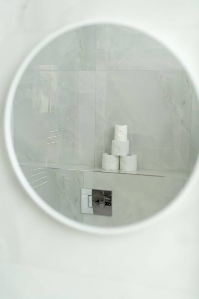 Mirror view of stacked toilet rolls in sleek marble-tiled bathroom.