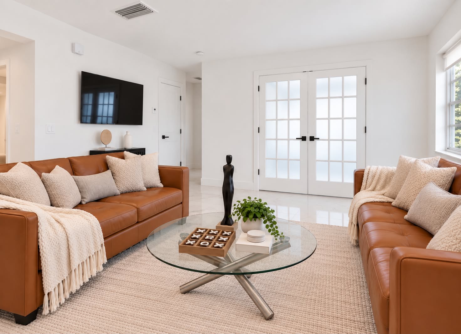 Bright modern lounge with leather sofas, TV, and elegant French doors
