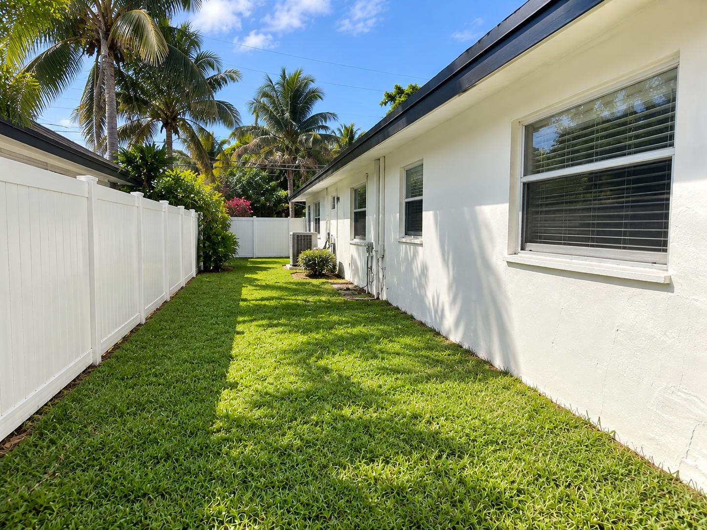 Private tropical side yard with lush lawn and bright privacy fencing