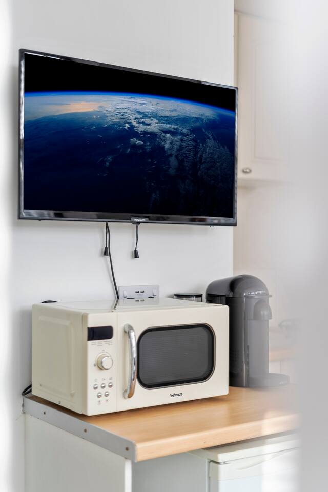 Compact kitchenette with microwave, coffee maker, and wall-mounted TV.