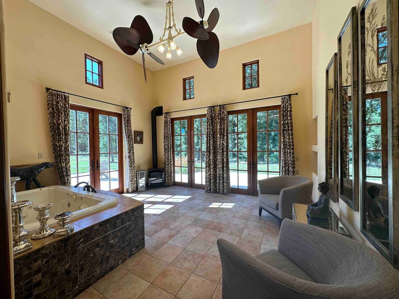Relax in this sunlit ensuite retreat featuring a spacious soaking tub, cozy seating area, and stunning views through elegant French doors.