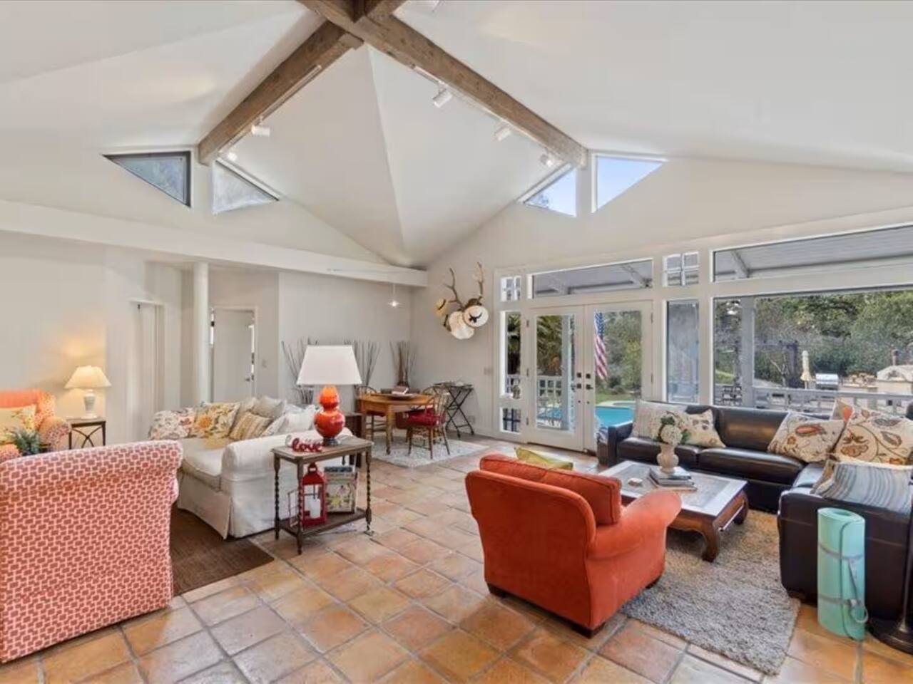Unwind in this inviting living room with soaring ceilings and plenty of seating, offering a perfect space to relax and enjoy breathtaking views of the pool and outdoor oasis through expansive glass doors and windows.