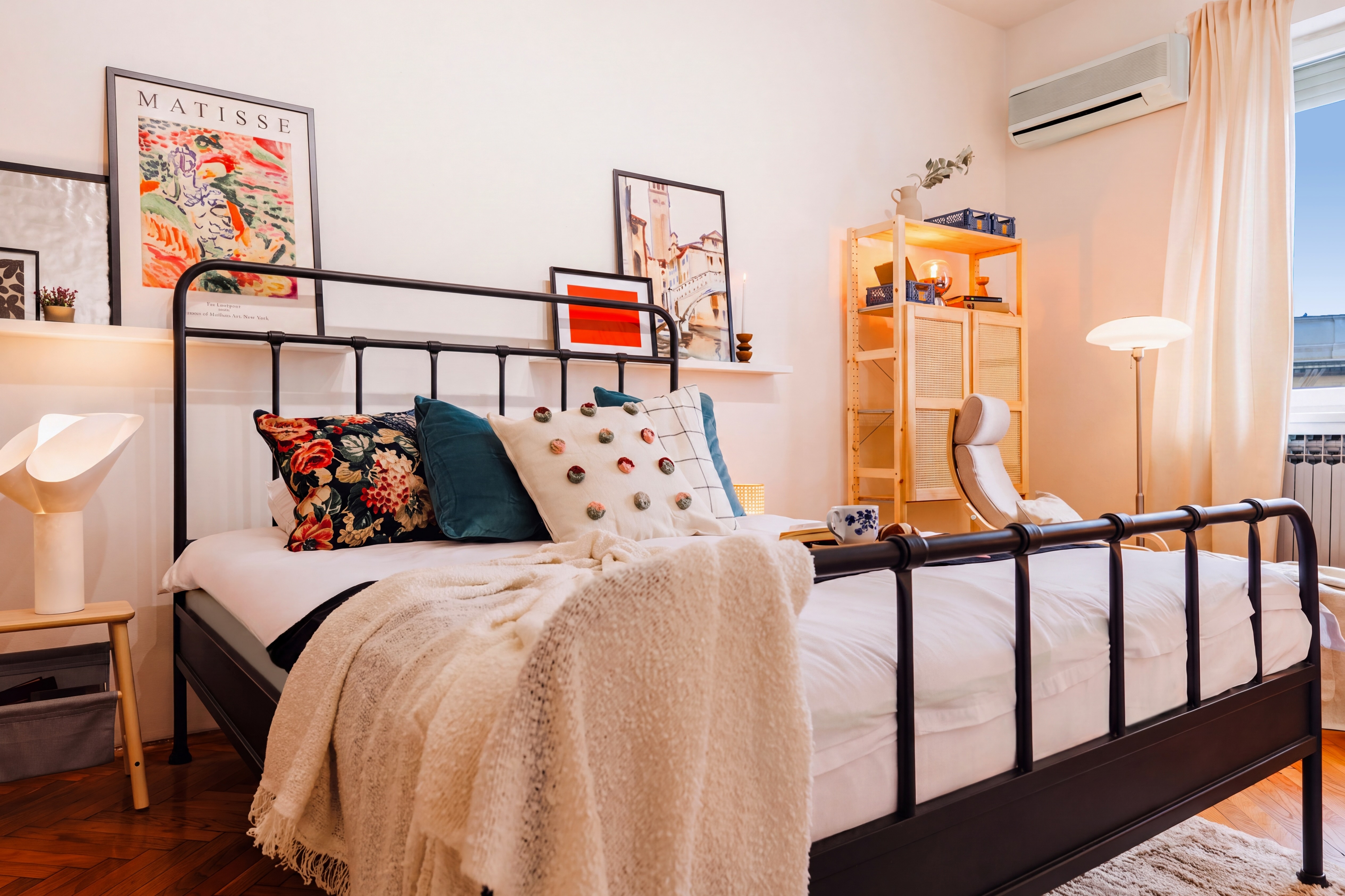 Bright, artful bedroom with cozy linens, soft lighting, and AC