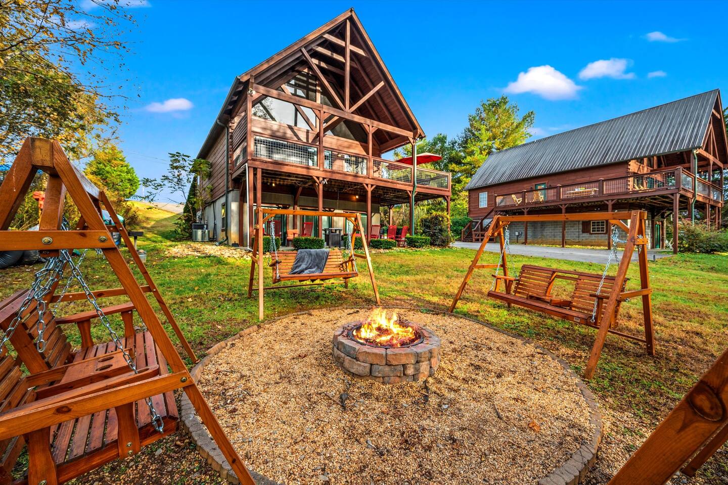 Fire pit on the lawn surrounded by wooden swinging benches, with the cabin behind