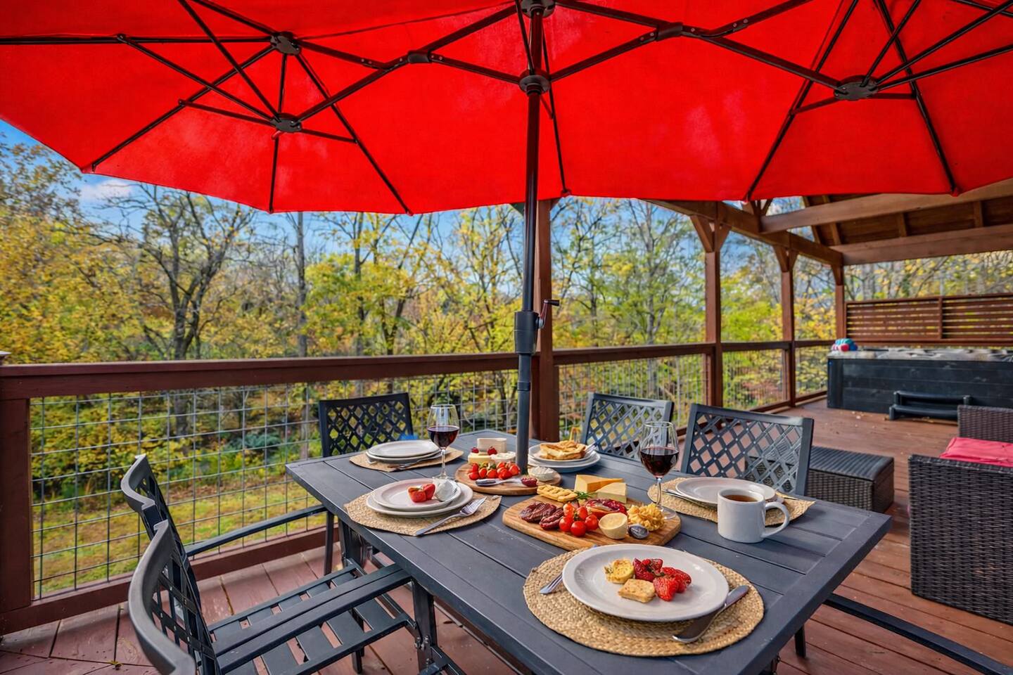 Balcony dining table set for a meal under a red umbrella, overlooking the trees