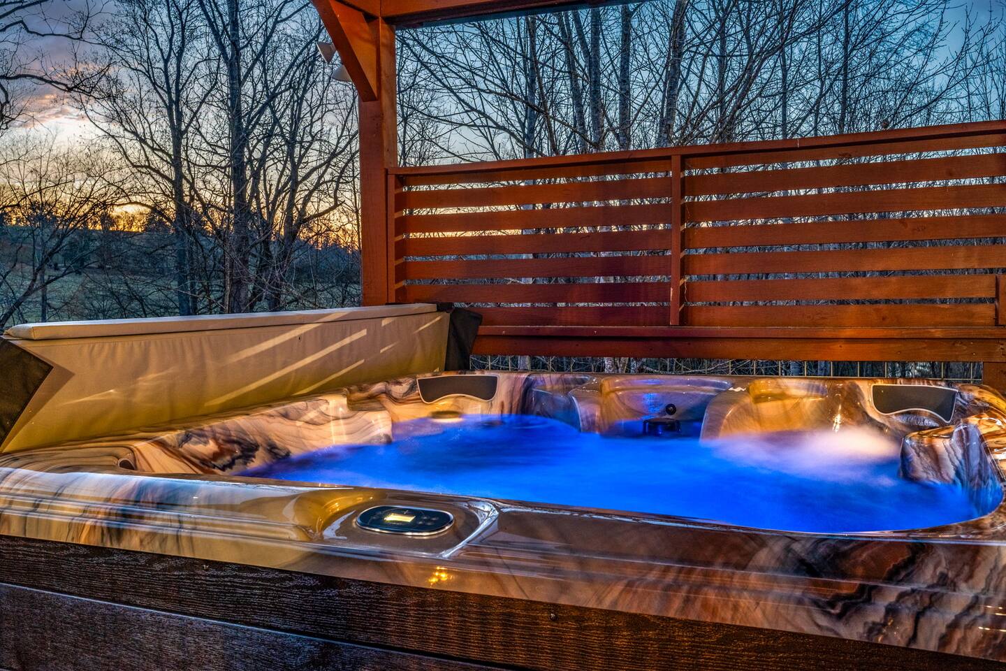 Hot tub glowing blue on the covered balcony at dusk, trees beyond