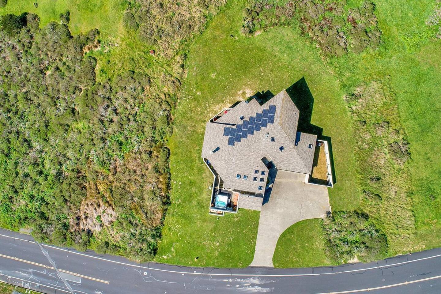 This overhead shot captures the property perched atop Dillon Hills, surrounded by lush greenery and open space. Its unique architecture, spacious driveway, and private hot tub make it a serene coastal retreat.
