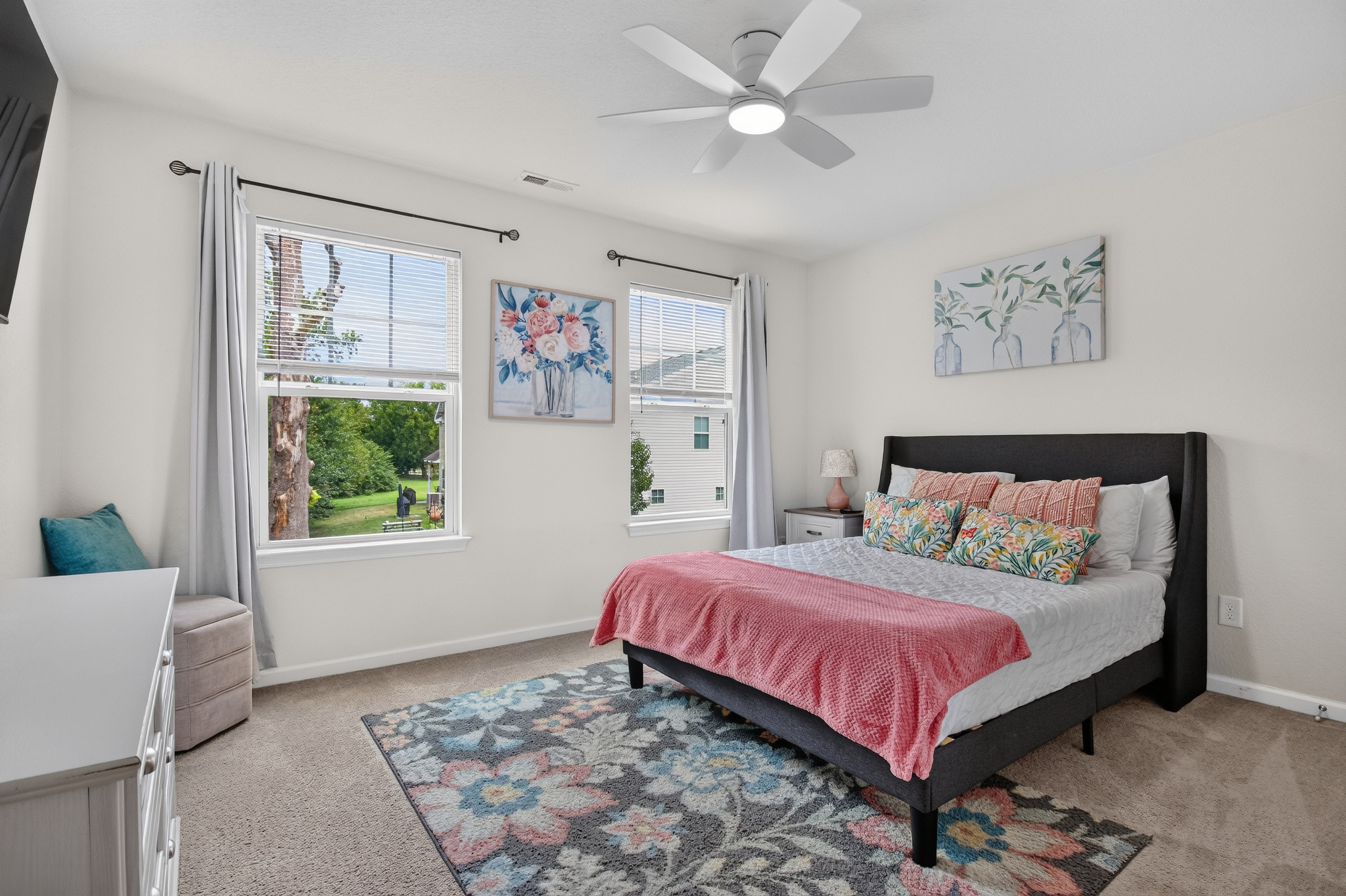 Bright, airy bedroom with floral decor, big windows, and a cozy plush bed
