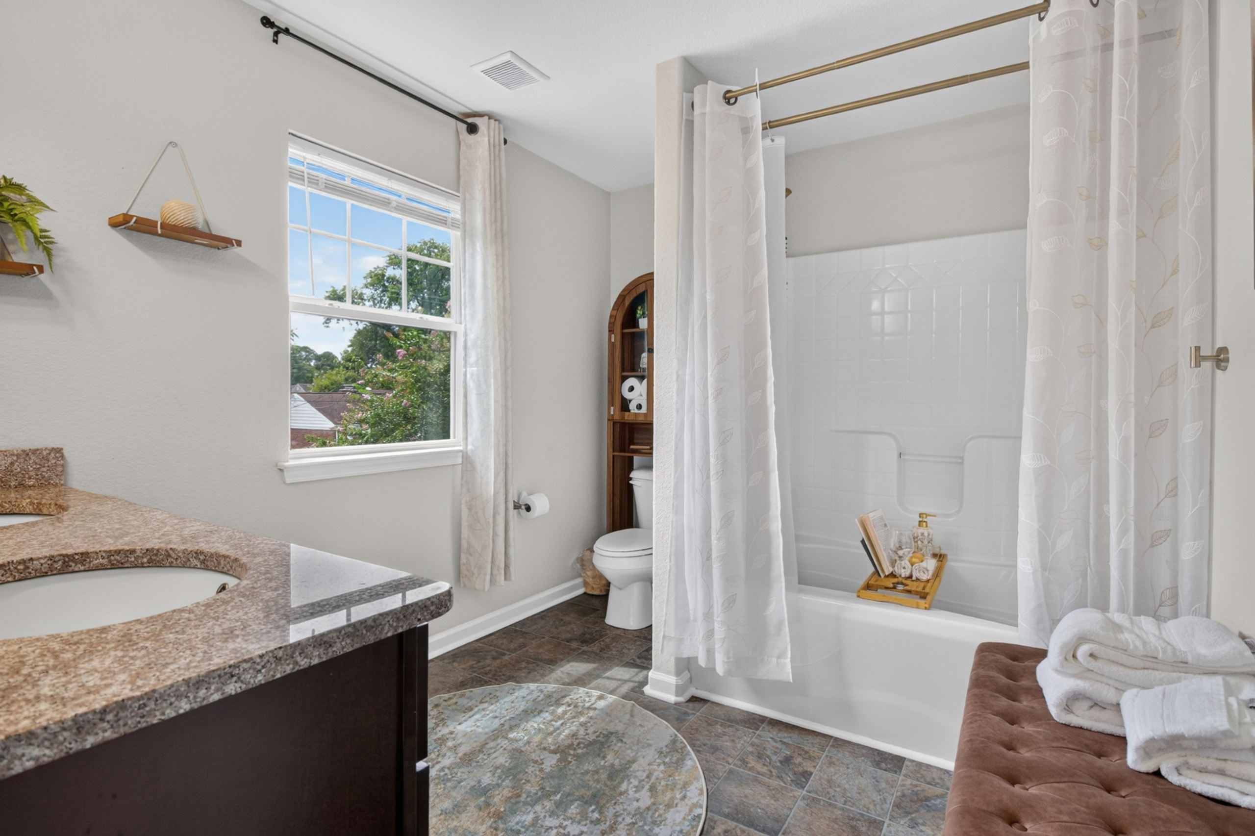 Bright spa-like bathroom with soaking tub, granite vanity, and natural light