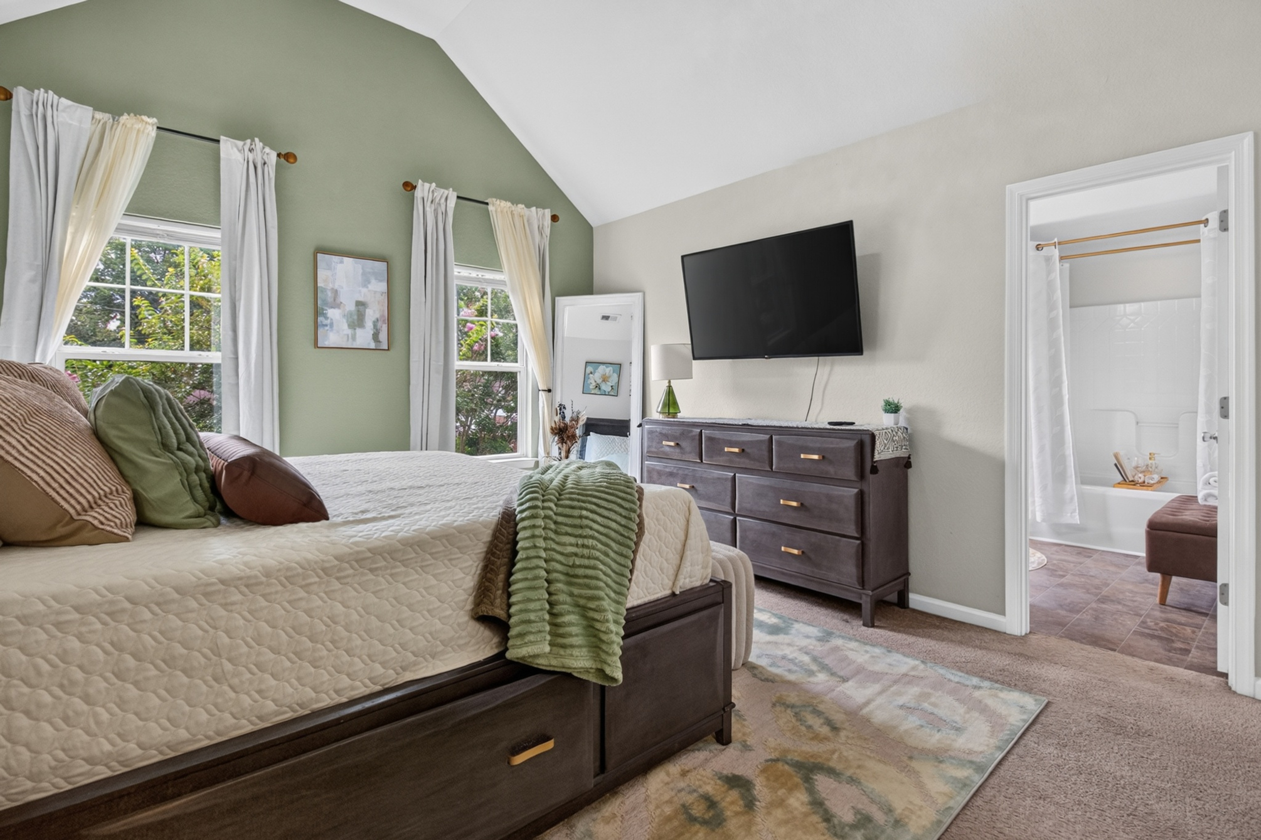 Bright king bedroom with vaulted ceiling, TV, and ensuite bath