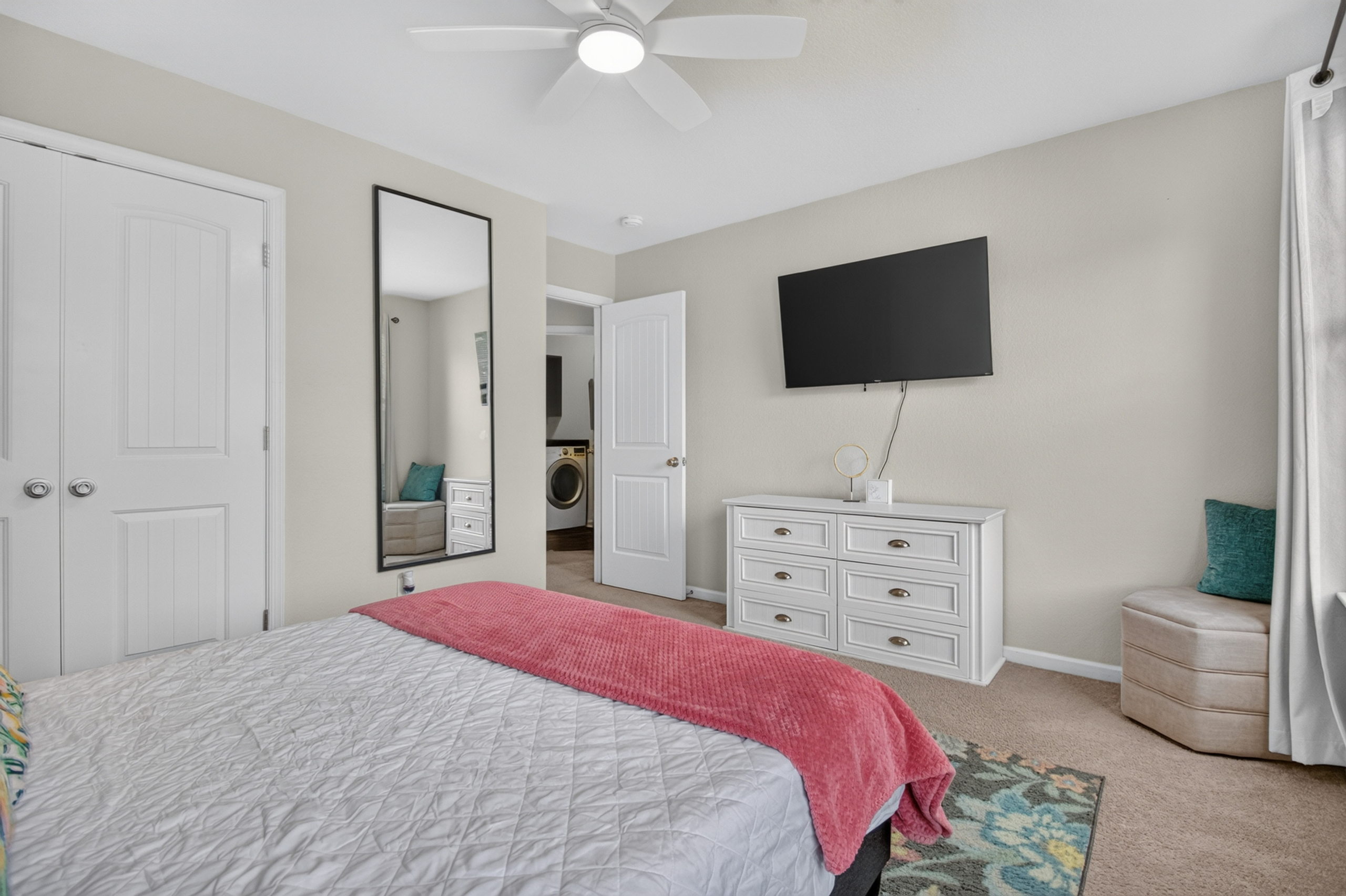 Bright bedroom with TV, dresser storage, and convenient in-home laundry