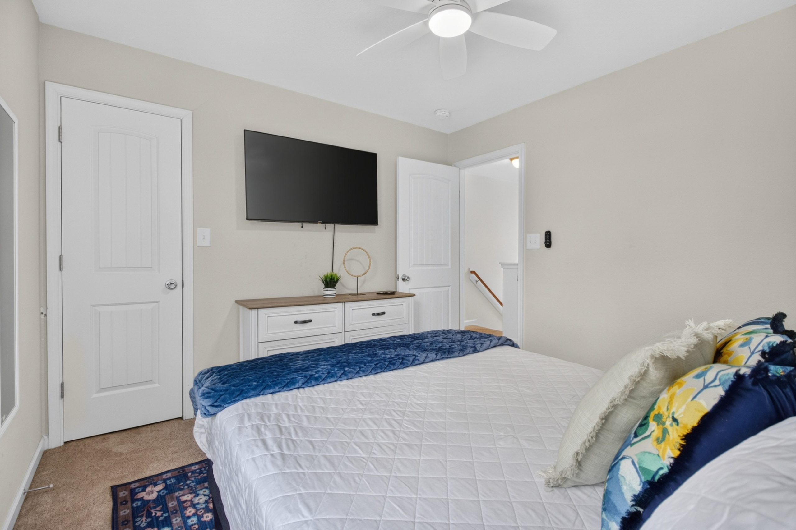 Cozy bedroom with wall-mounted TV, ceiling fan, and stylish decor