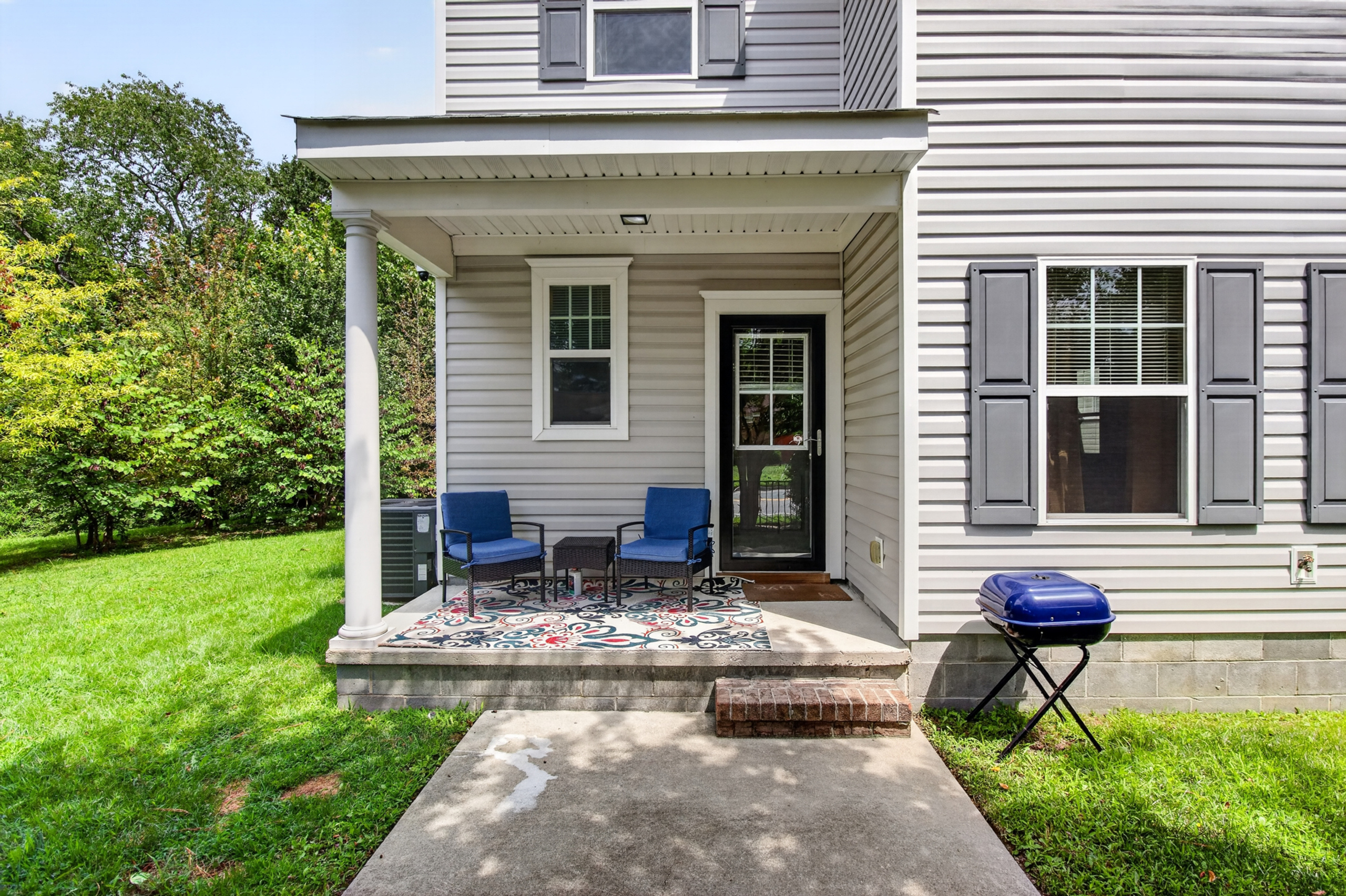 Covered front porch with seating, grill, and lush green yard