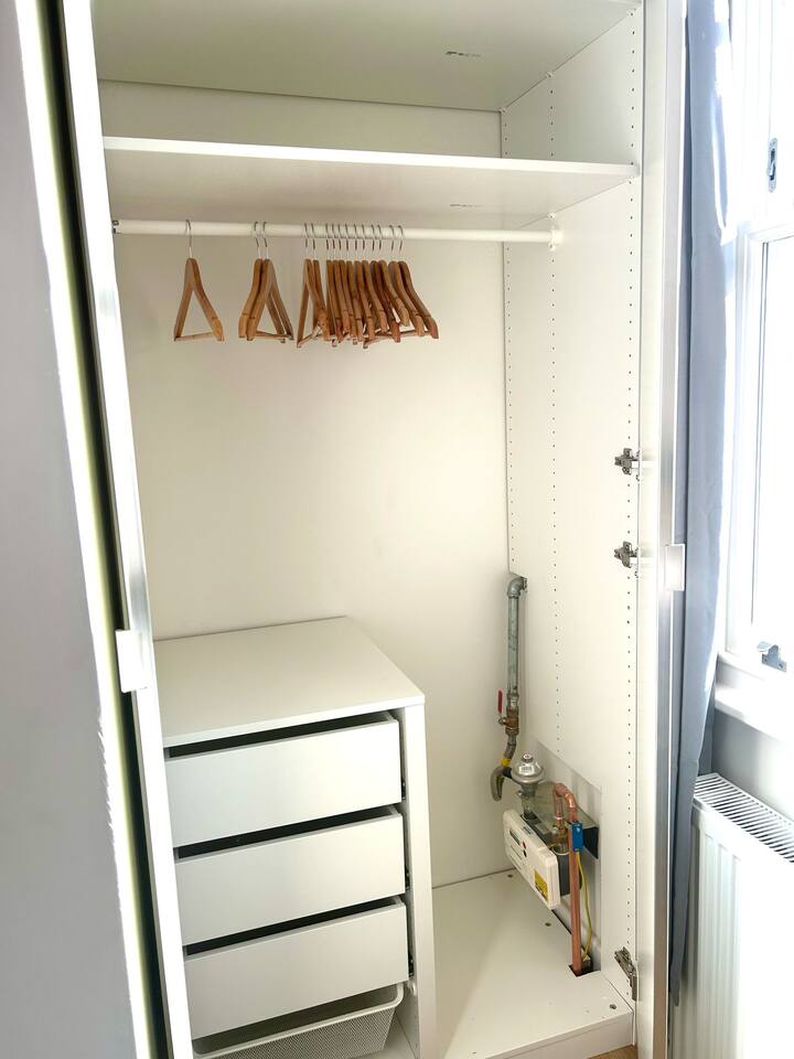 Find comfort in this bedroom at Wilton Road, Greater London, near Notting Hill, Acton, and Ealing. It comes with a double bed with yellow pillows, grey curtains, wooden floors, a yellow armchair, and floral wall art.