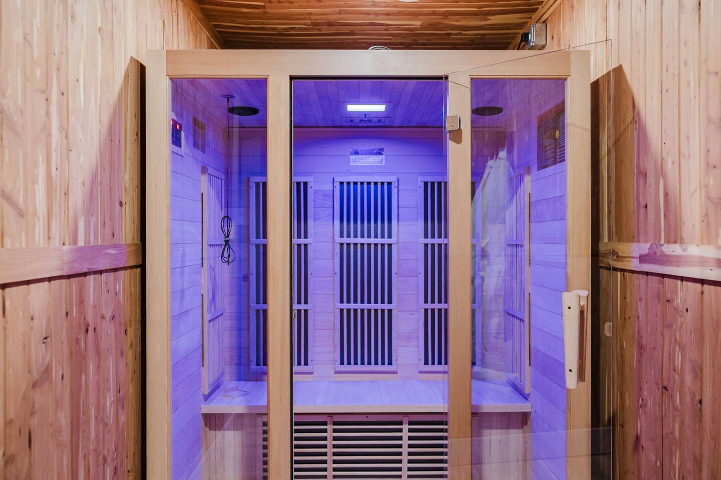 Infrared sauna lit purple, with cedar walls and glass doors