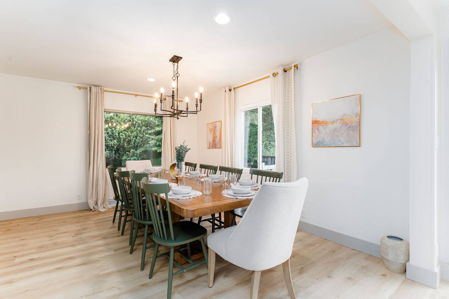 Dining table for a large group under a chandelier, with windows on two sides