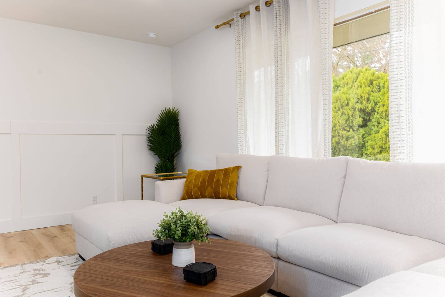 Bright living room with a white sectional, a round wood coffee table and tall windows