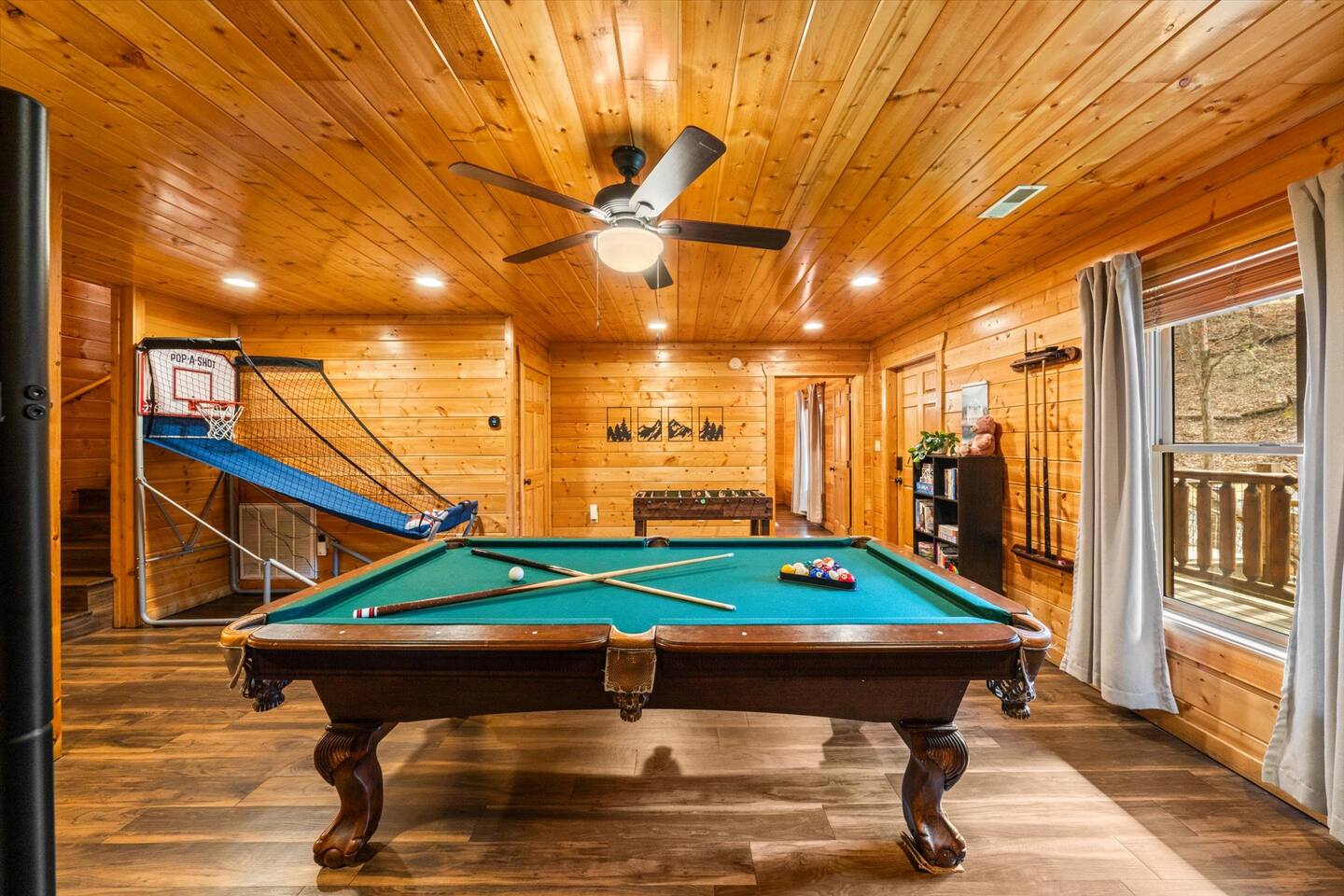 Pool table, pop-a-shot arcade game, foosball table, and bookshelf with childrens books, toys, and games