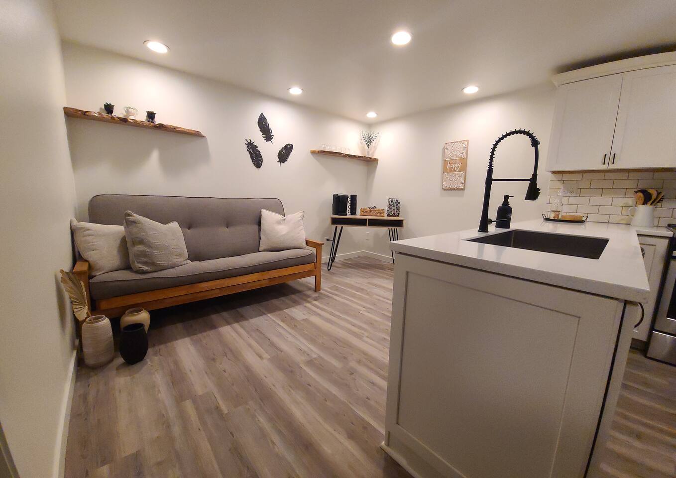 Bright, fully equipped kitchen with stainless-steel appliances, white cabinets, and ample counter space. Adjacent lounge area features a futon for extra sleeping. Ideal for cooking, relaxing, or hosting additional guests.