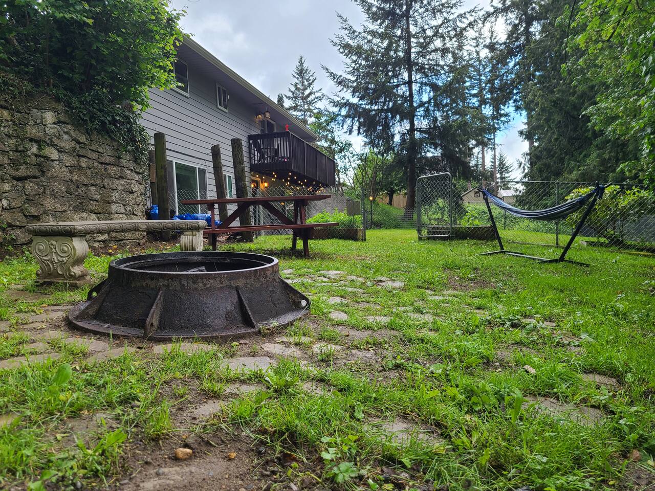 Enjoy the spacious backyard, perfect for relaxing or entertaining. Featuring a cozy fire pit, and a picnic table, this outdoor space is surrounded by lush greenery, offering a peaceful retreat under the open sky.