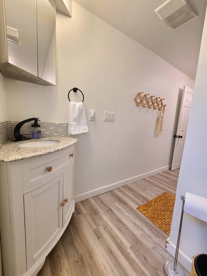 This bathroom combines modern design with comfort, featuring a walk-in shower with a stylish herringbone tile pattern, a granite countertop vanity, and chic wooden accents, perfect for a relaxing retreat.