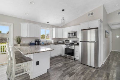 Stainless steel appliances throughout open kitchen with 3 bar seats, opening to elevated deck.