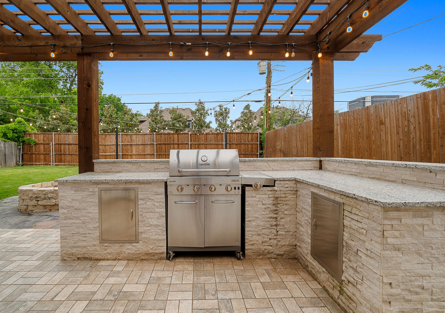 Covered outdoor kitchen with grill, granite counters, and string lights