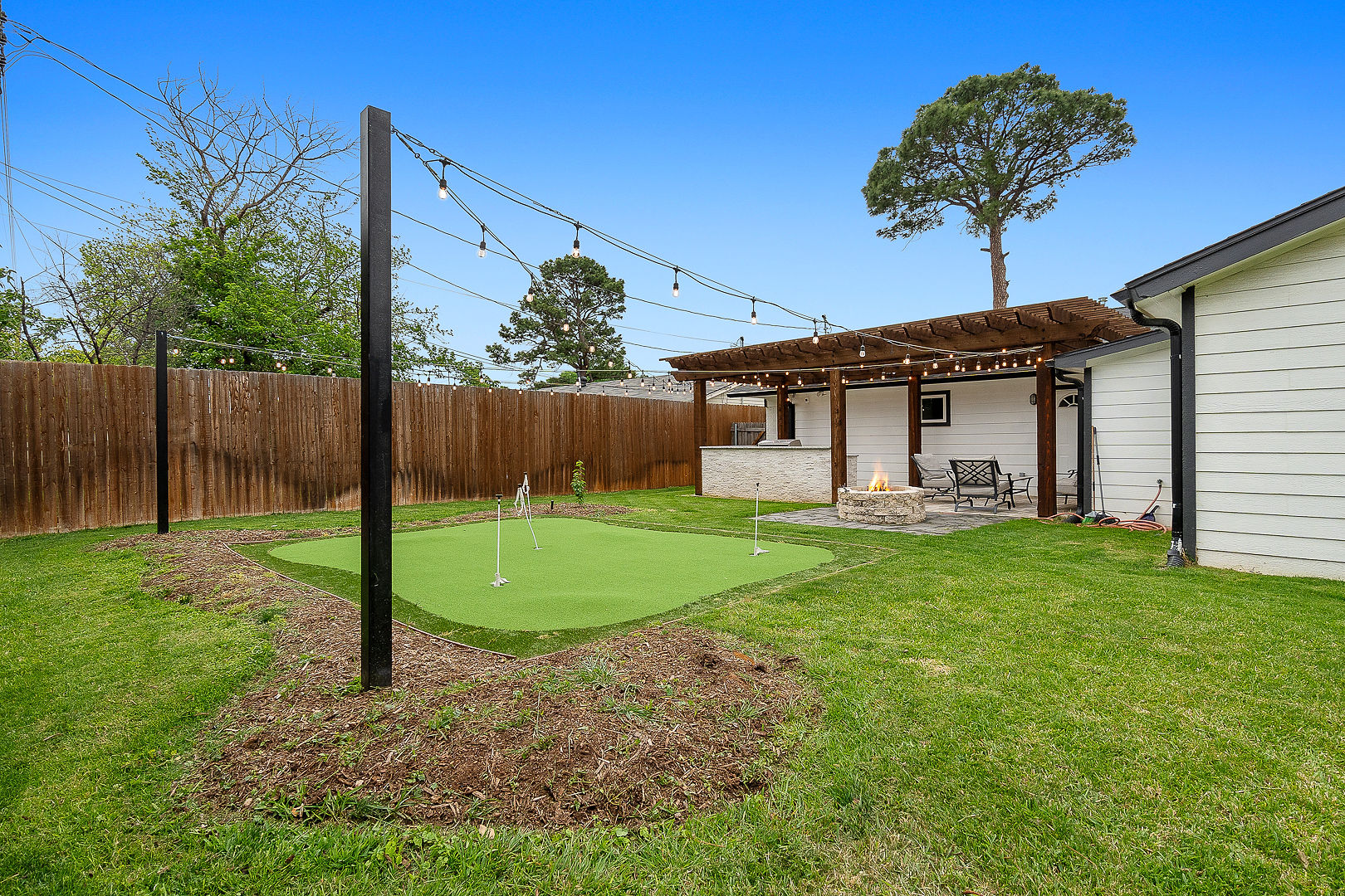 Private backyard with putting green, string lights, and cozy fire pit patio