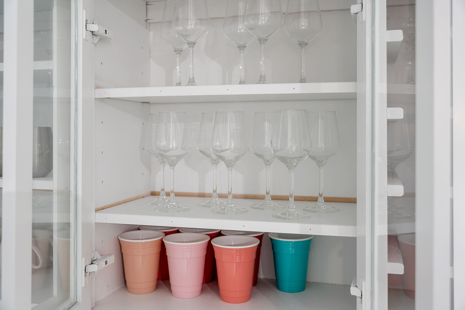 Well-stocked glassware cabinet with wine glasses and colorful cups