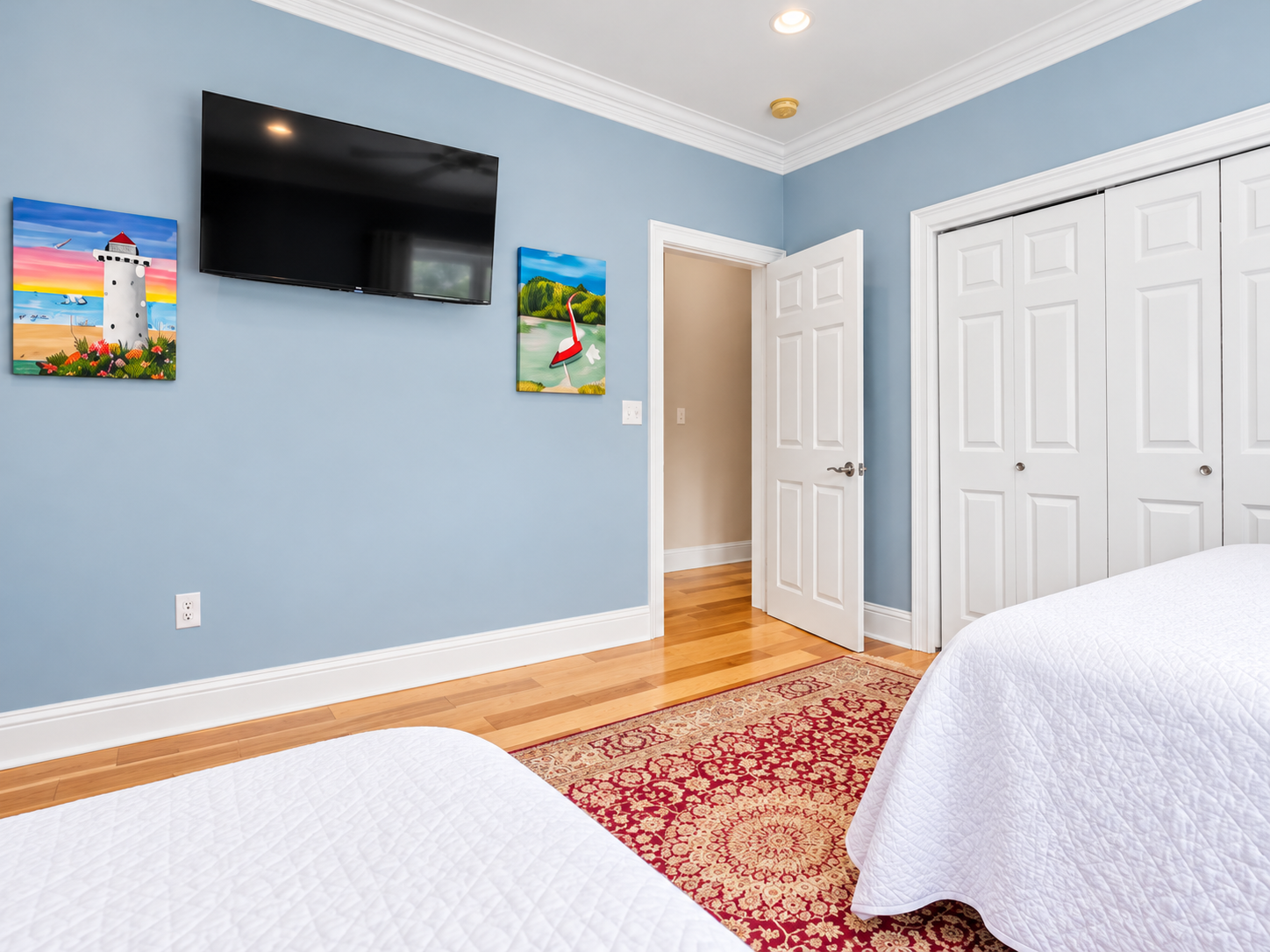 Bright coastal bedroom with hardwood floors, TV, and spacious storage
