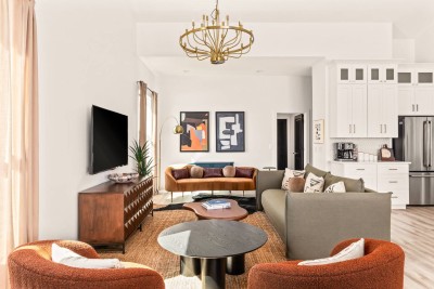 Bright, modern living room with cozy sofa, chic chairs, Smart TV, and bold art. Sunlight fills the space, highlighting the marble coffee table and stylish décor. Perfect for relaxing, movie nights, or gathering with friends. ✨