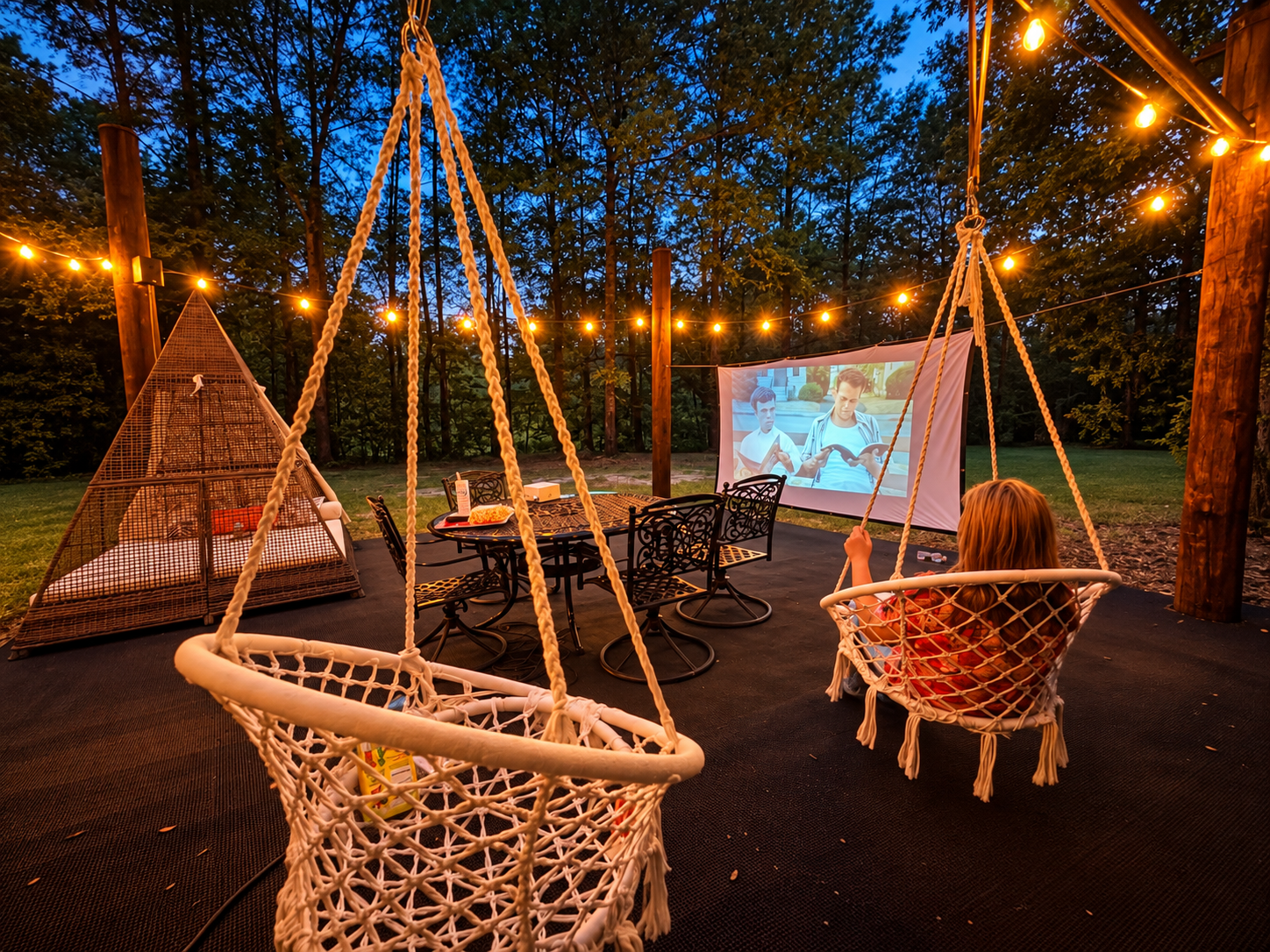 Cozy outdoor movie lounge with swing chairs and glowing string lights