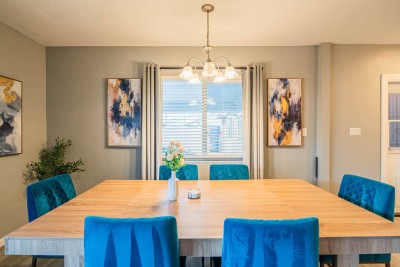 Spacious Dining Room. Gather around this large wooden dining table with plush velvet blue chairs for a pop of color! Perfect for a formal meal. Bright window and stylish art create an inviting atmosphere. Room for the whole group!