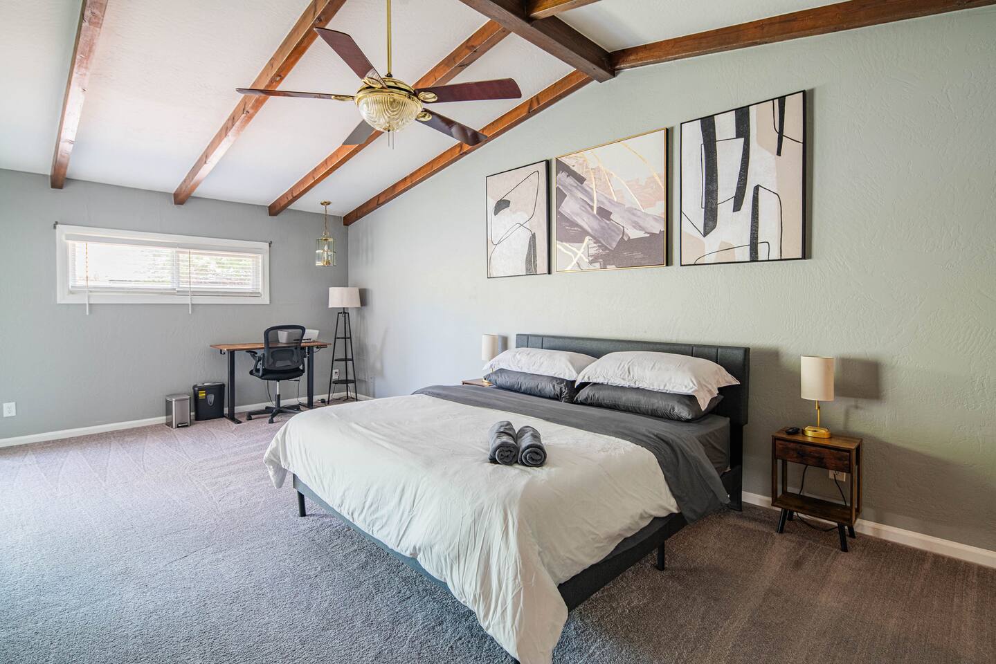 Stunning Vaulted Primary Bedroom! Sleep soundly in the King-sized bed beneath vaulted ceilings with exposed wood beams and a ceiling fan. This huge room includes a dedicated desk workspace and large windows.