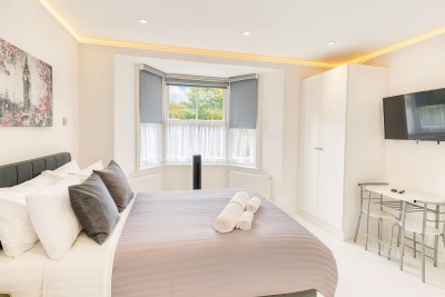 Bright, airy bedroom featuring a large bay window and a sleek wall-mounted TV.
