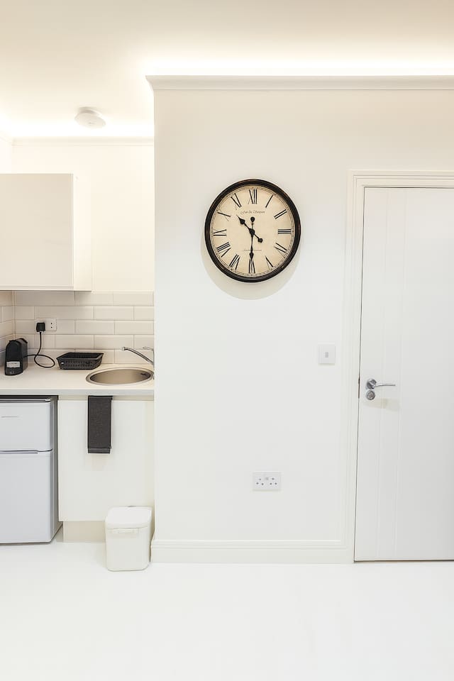 Compact kitchenette with sink, mini fridge, kettle & stylish clock. Clean & functional!