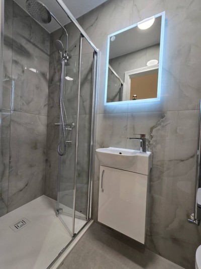 Sleek bathroom with a glass walk-in rainfall shower and glowing LED mirror.
