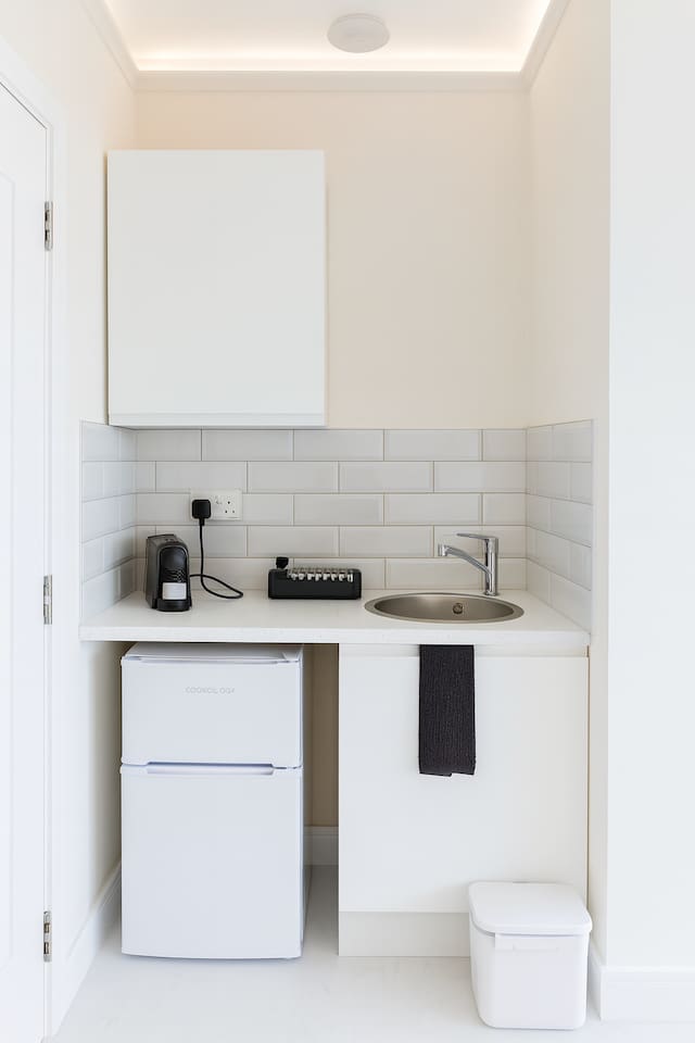 Compact kitchenette featuring a mini-fridge, coffee station, and sleek tiling.