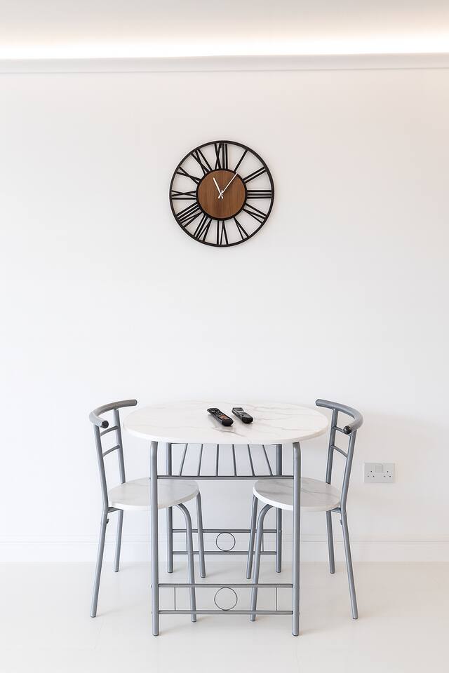 Minimal dining nook with cozy seating, modern clock, and bright clean style.