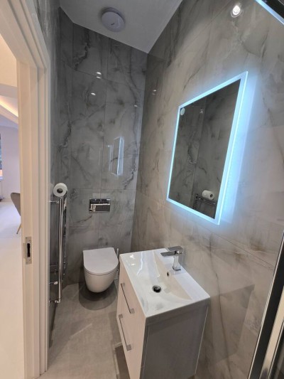 Modern, sun-drenched studio with a plush bed, dining area, and leafy garden views.