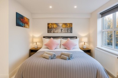 Modern, minimalist bedroom featuring a plush bed and large sunlit window.