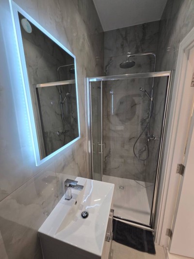 Modern, marble-tiled bathroom with a rainfall shower and glowing LED mirror.