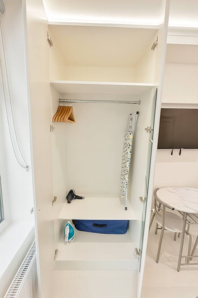 Neat wardrobe with hangers, iron, hairdryer, and suitcase for guest convenience.