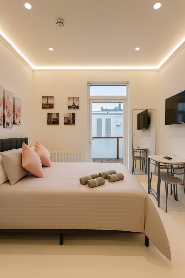 Bright, modern studio with a plush bed, dining area, and access to a sunny balcony.
