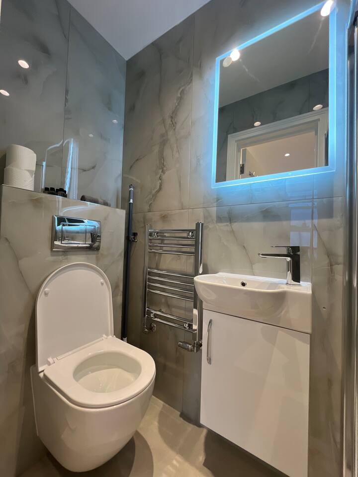 Stylish marble bathroom with LED mirror, vanity, and modern wall-mounted toilet.