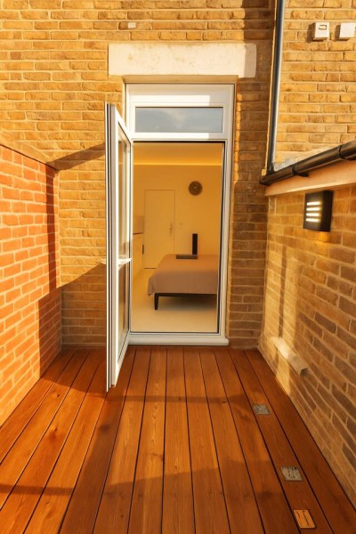Cozy balcony with wooden flooring, glass doors, and warm-lit bedroom inside.